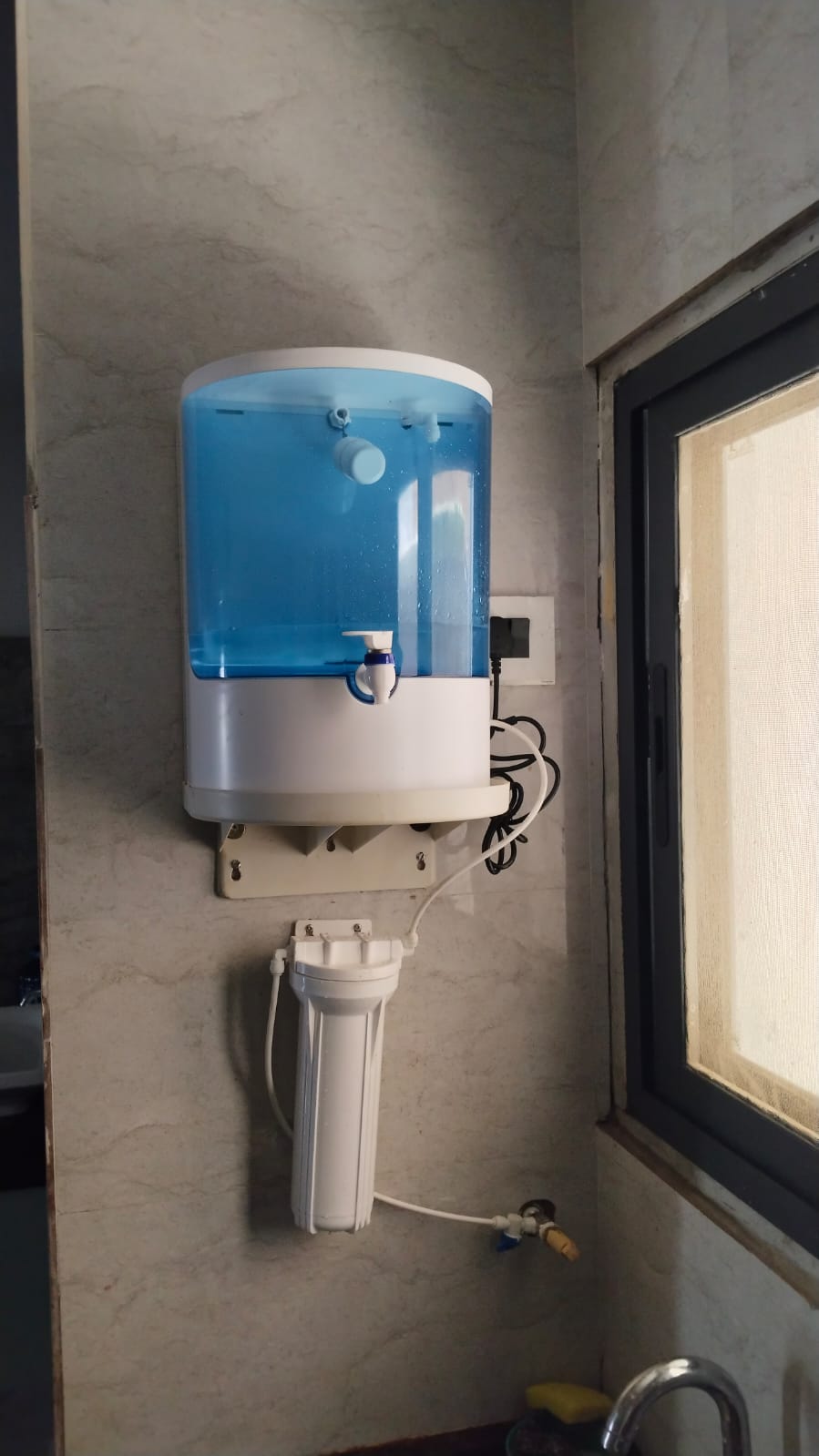Domestic RO water purifier with transparent tank installed in a kitchen corner